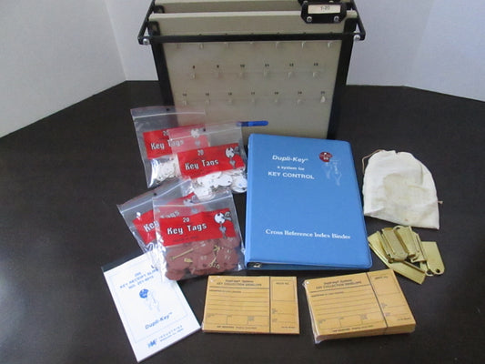 A metal file rack with 40 key slots, a blue dupli-key cover, and various accessories laid out in front, including packaging and a key tag.