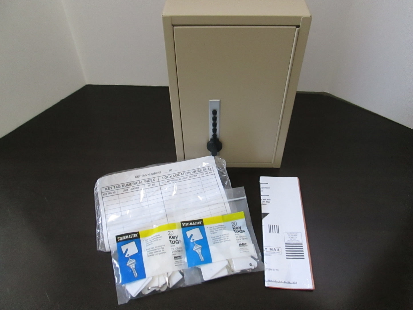 A beige metal 30 key storage cabinet with a Simplex combination lock, accompanied by packaged key tags and mounting hardware.