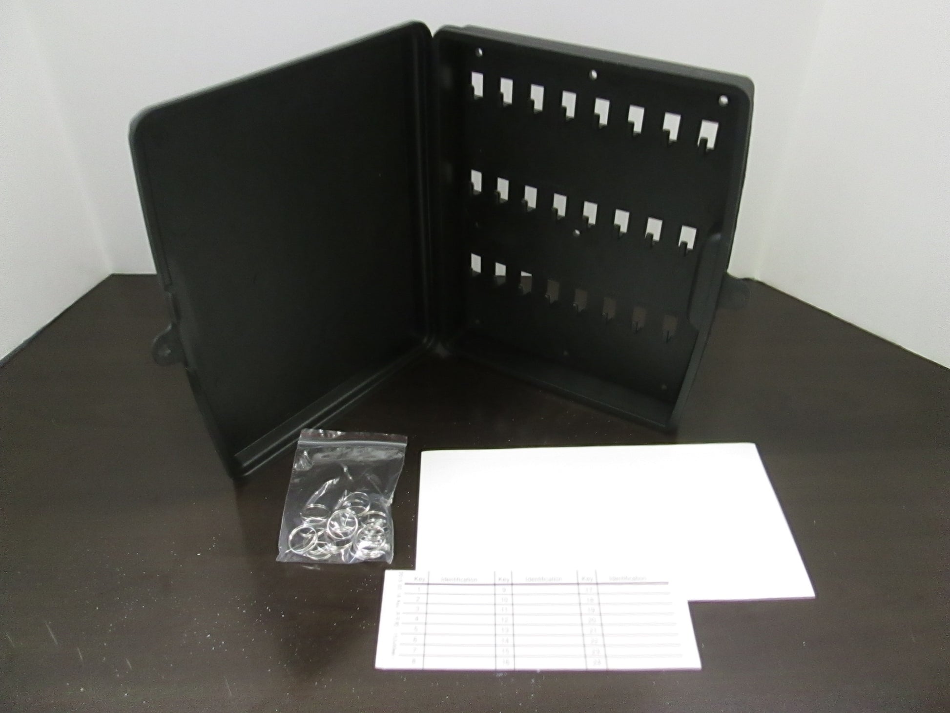 A black polyethelene key cabinet with 24 key rings, key tags, and an identification chart, alongside predrilled holes and mounting screws.